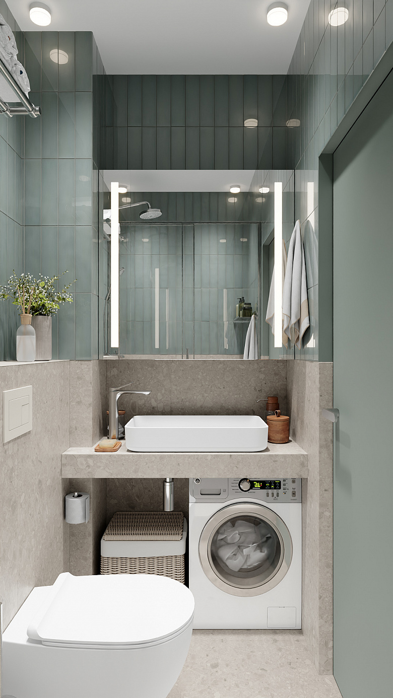 фото:Современная компактная ванная в минималистичном стиле: серо-зелёная плитка на стенах создаёт спокойный фон, столешница под раковину имитирует натуральный камень. Центральные элементы — лаконичная прямоугольная раковина, стильная стиральная машина под ней и навесной унитаз. Большое зеркало с подсветкой визуально расширяет пространство. Акценты — плетёная корзина для белья, деревянные аксессуары и ваза с сухоцветами. Чистые линии, функциональность и гармония оттенков делают интерьер практичным и уютным