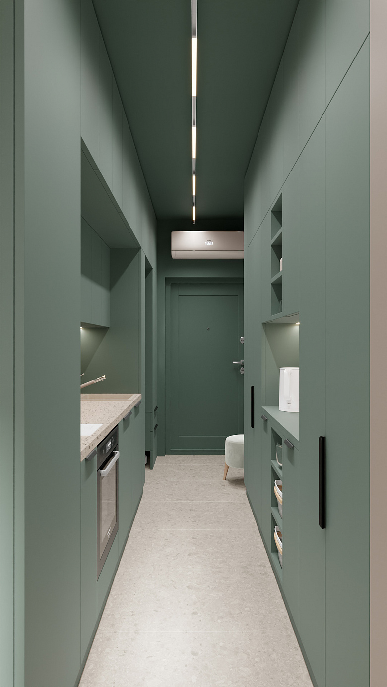 фото:Узкая кухня-коридор в минималистичном стиле: доминирует глубокий зелёный цвет фасадов и стен, создающий ощущение уюта и спокойствия. Встроенные шкафы по обеим сторонам, лаконичные чёрные ручки подчёркивают современность. Слева — компактная кухонная зона с мойкой и встроенной духовкой, справа — открытые полки с посудой и закрытыми секциями для хранения. Дополнительный элемент — небольшой пуф у двери, создающий уюта. Линейное потолочное освещение равномерно заливает пространство мягким светом. Чистые линии, функциональность, гармония оттенков — идеальный баланс для компактного пространства